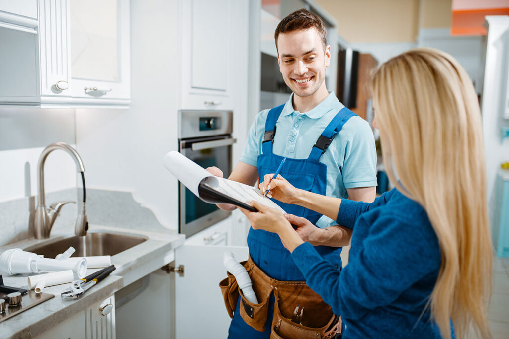 A male plumber standing in a kitchen with a client looking over a quote