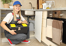 A female plumber smiling as she wears protective overalls and holds a toolbox