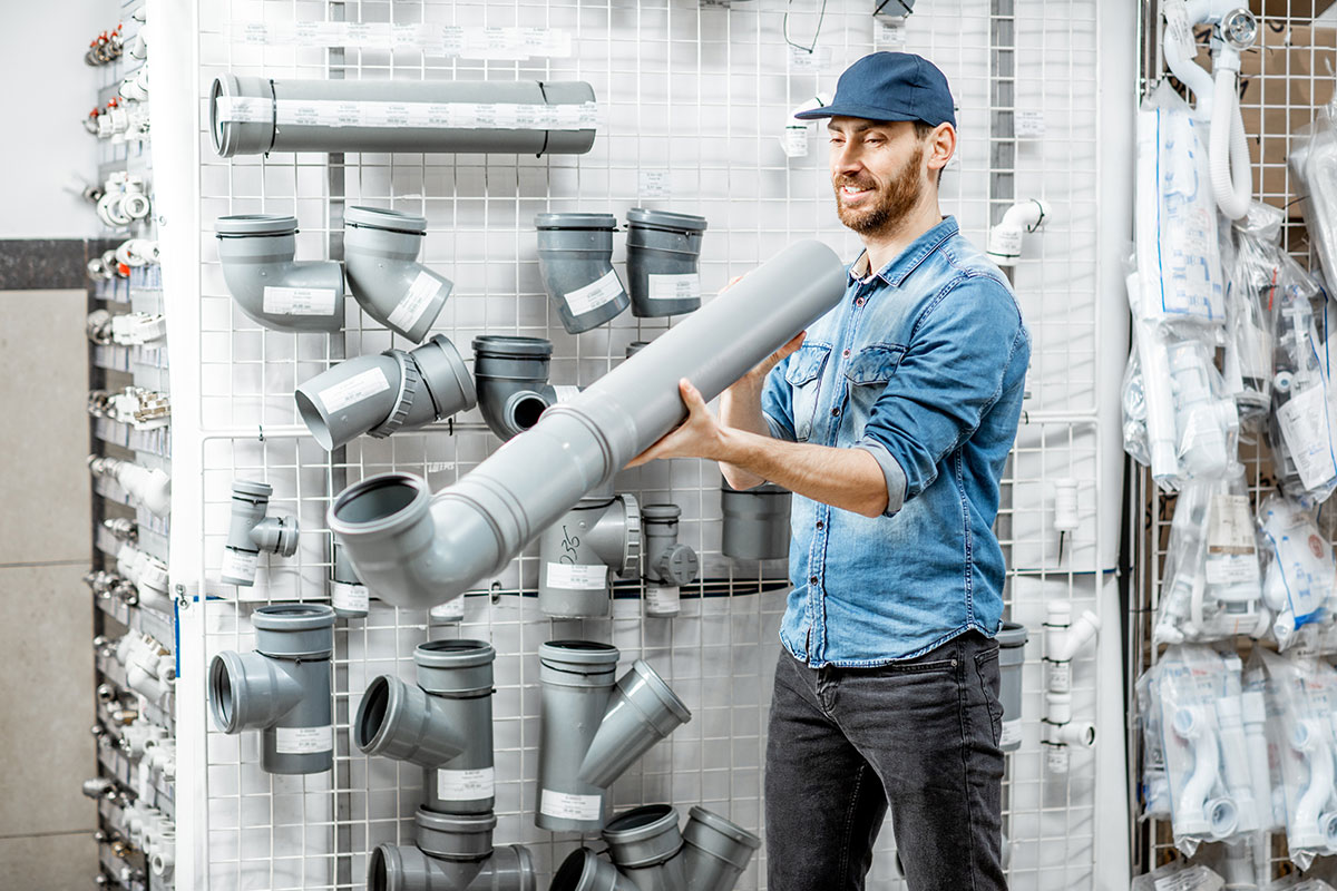 A male plumber smiling as he stands in a store and holds and looks at a big drain pipe