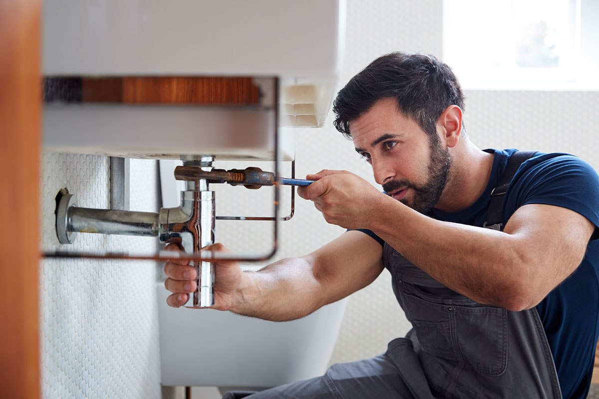 A male plumber sitting beneath a sink and completing repairs in a residential washroom