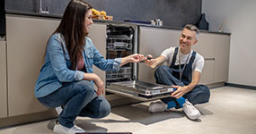 A male plumber smiling as he completes service on a dishwasher and receives something from the client